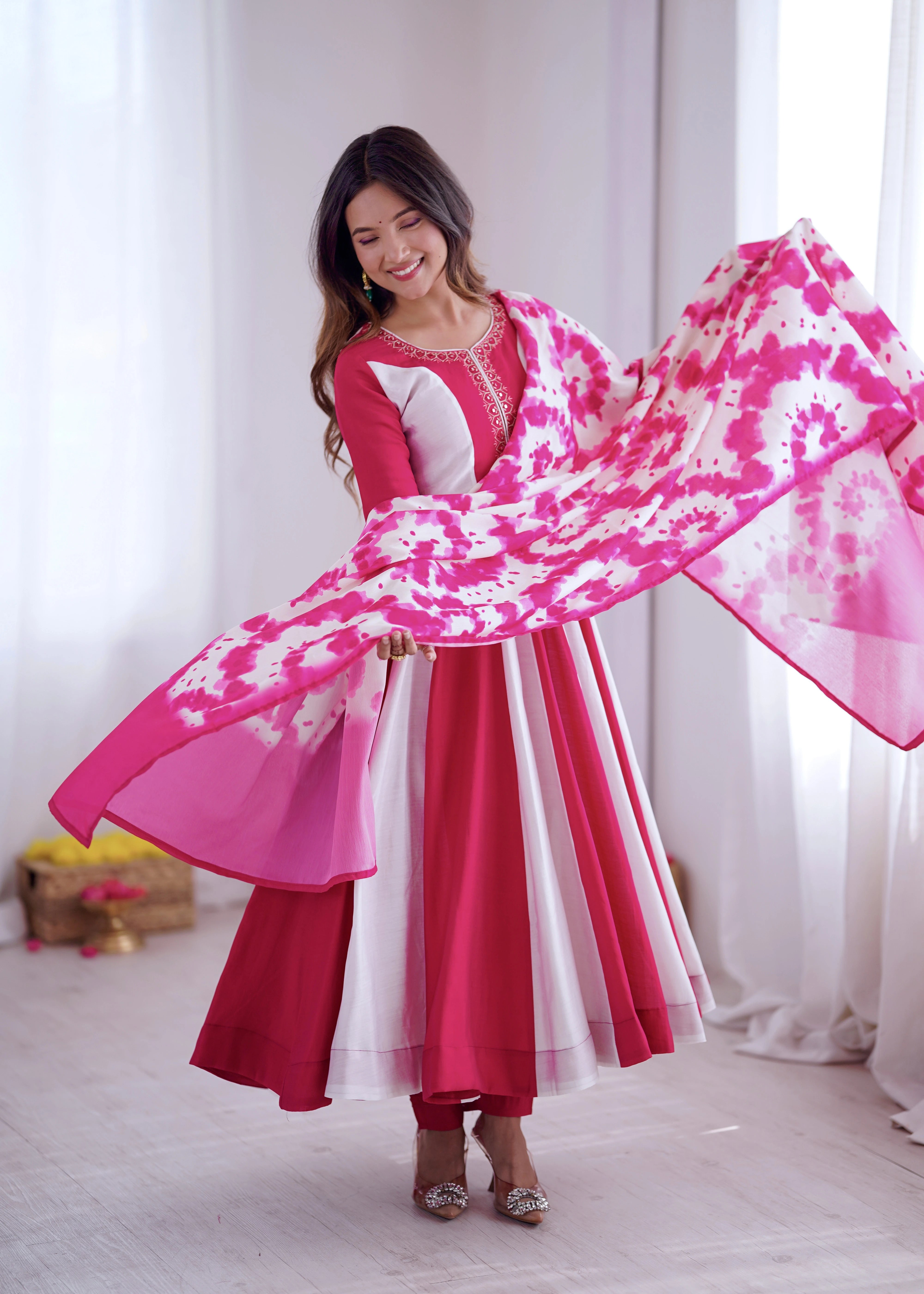 Woman in a pink and white traditional outfit with a matching scarf, standing indoors.